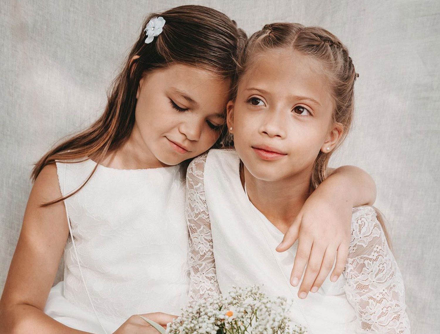 Zwei Mädchen in Kommunionkleidern sitzen nebeneinander