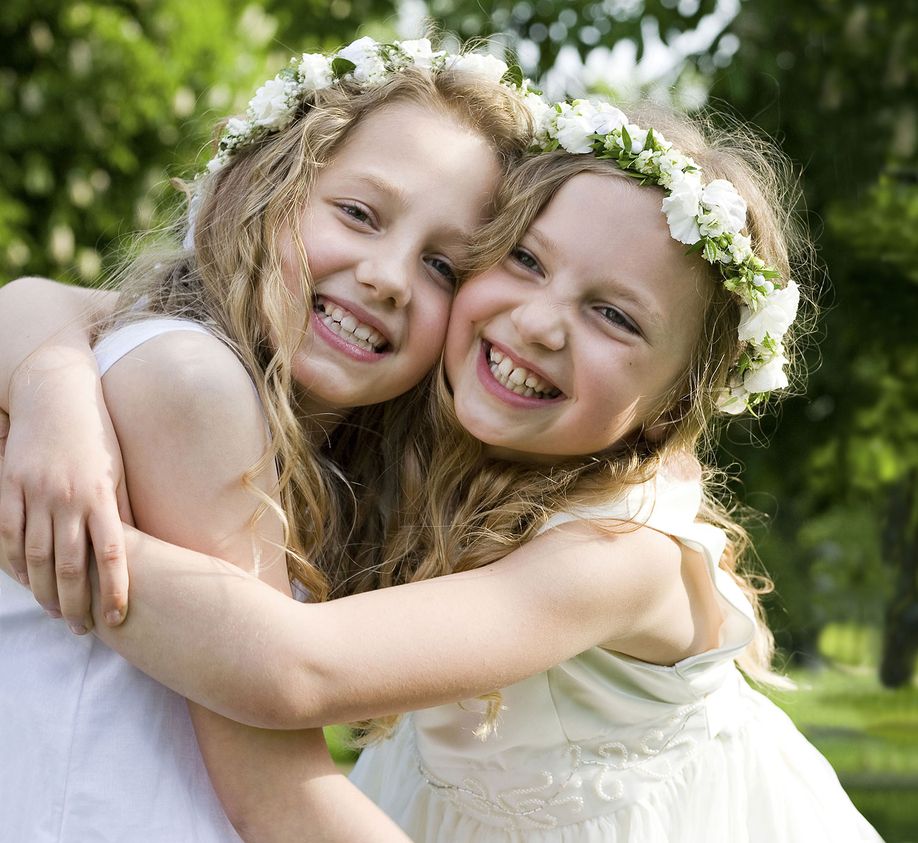 Zwei glückliche Mädchen in Kommunionkleidern umarmen sich